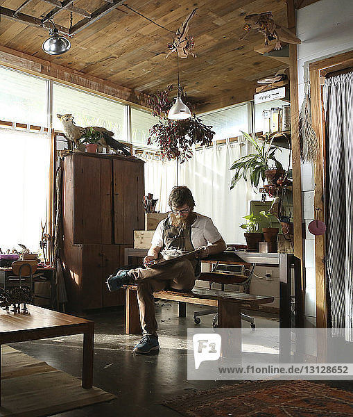 Tischler liest Dokument in voller Länge  während er in der Werkstatt auf einer Bank sitzt