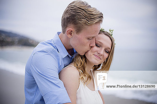 Mann küsst Freundin  während er am Strand gegen den Himmel steht