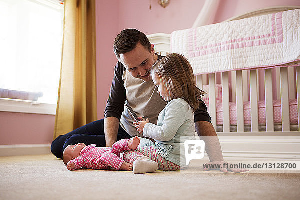 Happy man looking at daughter using mobile phone while sitting on floor at home