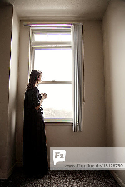 Side view of woman looking away while standing by window at home