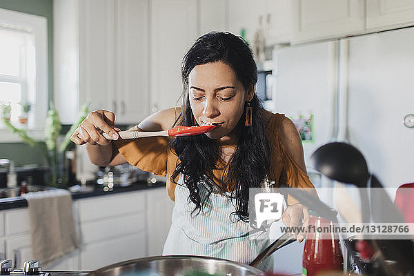 Woman smelling food on spatula at kitchen