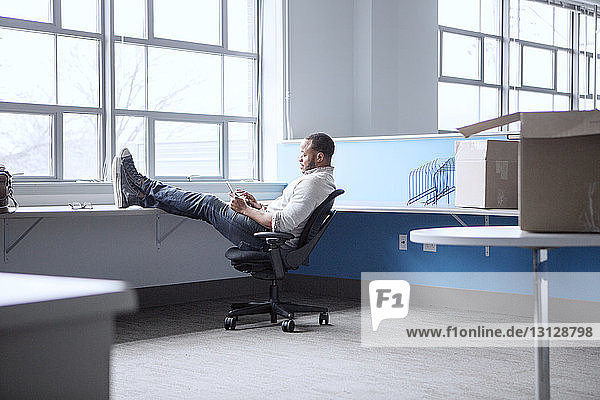 Businessman using mobile phone while relaxing on chair in office