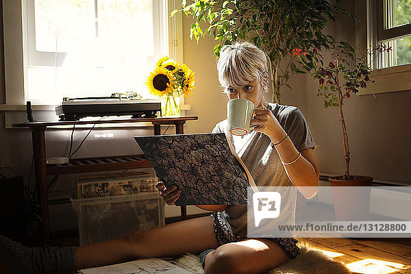 Junge Frau trinkt Kaffee  während sie sich zu Hause eine Schallplatte ansieht