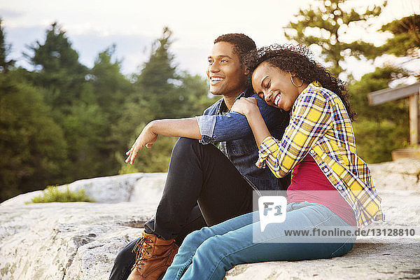Glückliches Paar sitzt auf einem Felsen mit Bäumen im Hintergrund