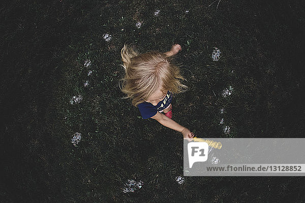 High angle view of girl playing with bubble wand on grassy field in backyard