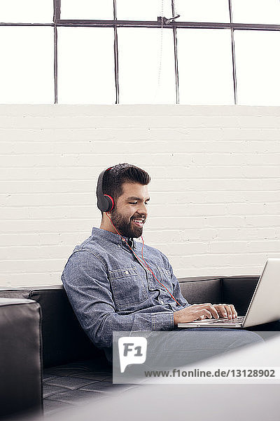 Smiling man wearing headphones using laptop while sitting at creative office