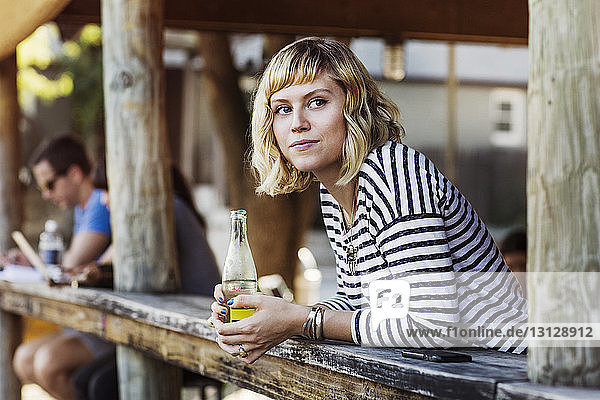 Woman holding soda bottle while leaning on table in cafe