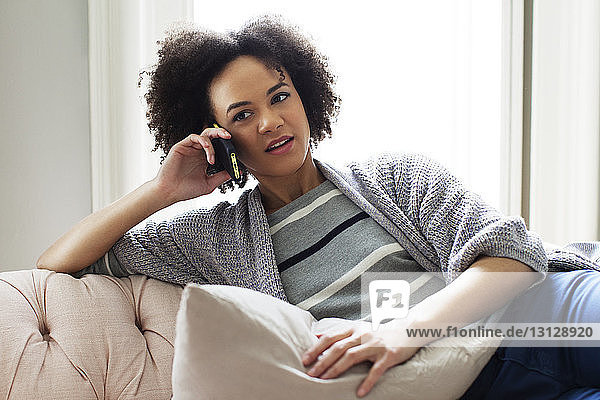 Frau benutzt Smartphone  während sie sich zu Hause auf dem Sofa entspannt