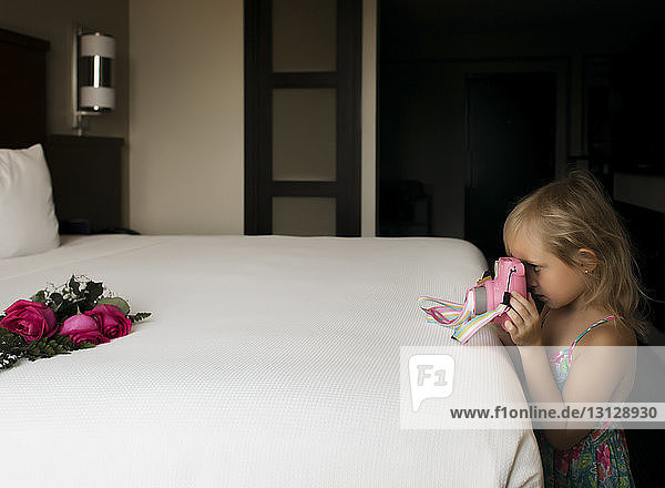 Side view of girl photographing roses on bed at home
