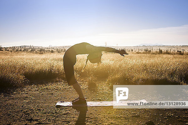 Side view of young woman practicing yoga on exercise mat in field