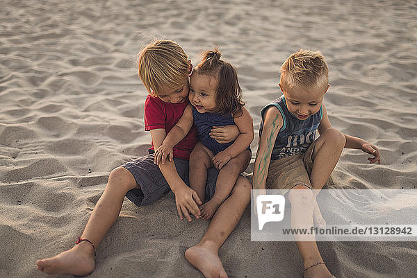 Siblings sitting on sand at beach