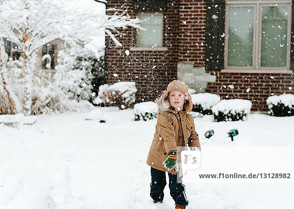 Süßer Junge spielt mit Schnee im Hof