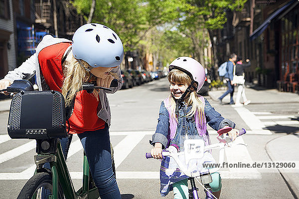 Glückliche Frau spricht mit ihrer Tochter beim Fahrradfahren auf der Straße
