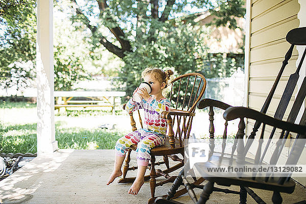 Mädchen trinkt  während sie auf einem Schaukelstuhl auf der Veranda sitzt