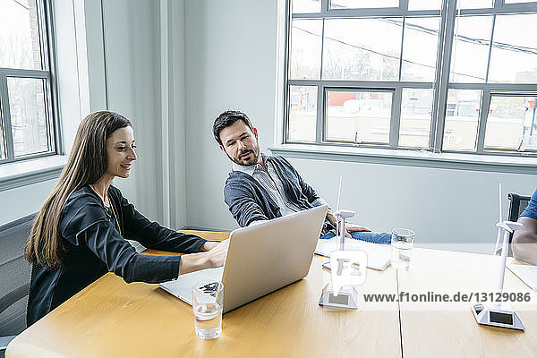 Businesswoman showing laptop computer to colleague while sitting in board room
