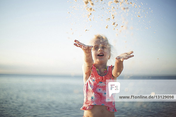 Cheerful girl playing with sand against sea at beach