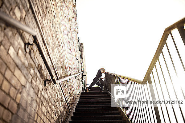 Weibliche Sportlerin übt auf einer Treppe an einer Wand gegen den klaren Himmel