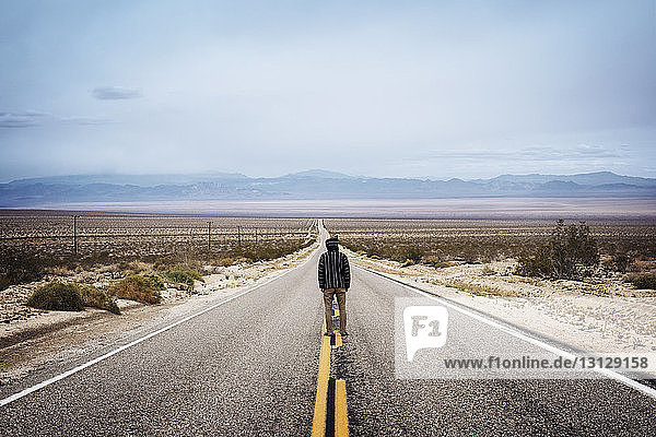 Rear view of man standing on empty highway looking towards horizon