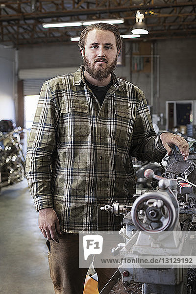 Porträt eines Mechanikers  der in einer Autowerkstatt an einer Maschine steht