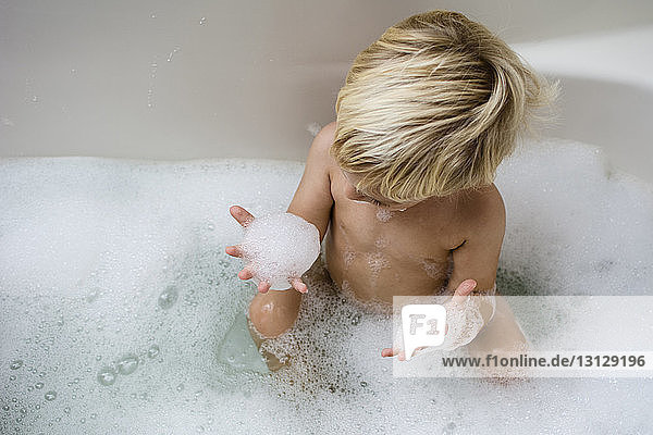 Schrägaufnahme eines Jungen  der beim Baden in der Badewanne mit Seifenlauge spielt