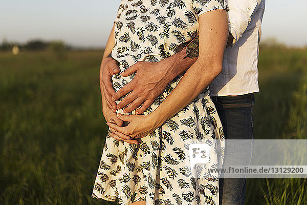 Midsection of man touching PRegnant woman's stomach while standing on grassy field