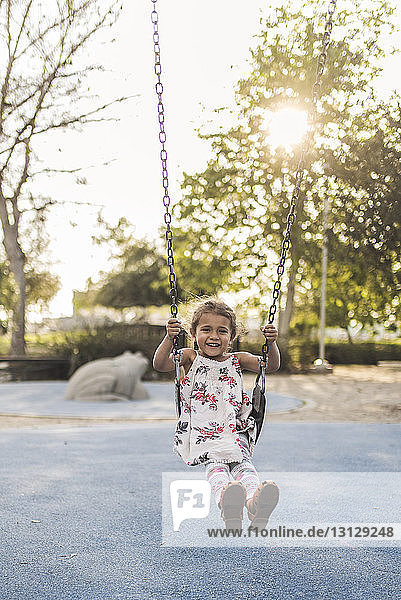 Porträt eines glücklichen Mädchens  das sich auf dem Spielplatz gegen den Himmel schwingt