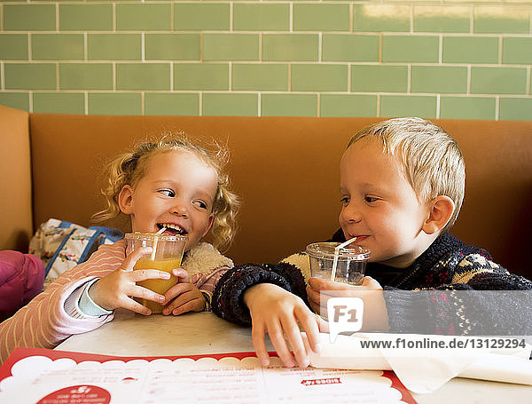 Glückliche Geschwister trinken Saft  während sie im Restaurant sitzen