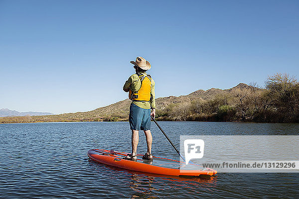 Rückansicht eines Mannes beim Paddeln auf einem See vor klarem blauen Himmel