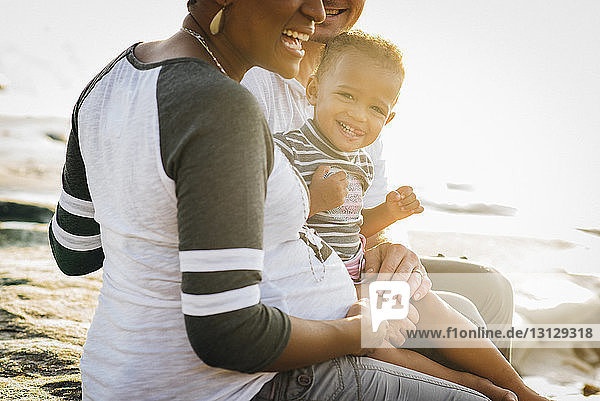 Porträt einer glücklichen Tochter mit am Strand sitzenden Eltern