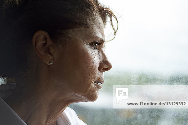 Nachdenkliche Frau schaut durch Fenster  während sie zu Hause steht