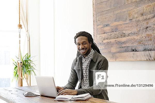 Portrait of happy young businessman working on laptop in creative office