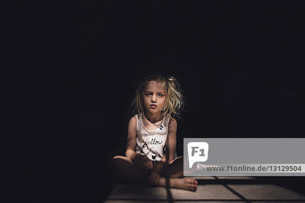 Portrait of thoughtful girl sitting on floor in darkroom during sunny day