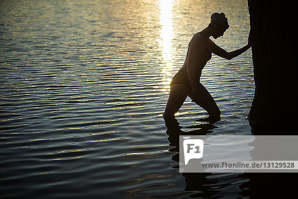 Seitenansicht einer Schwimmerin  die sich bei Sonnenuntergang am Baum im See ausruht