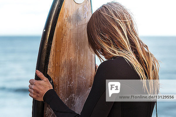 Frau trägt Neoprenanzug  während sie am Strand ein Surfbrett hält