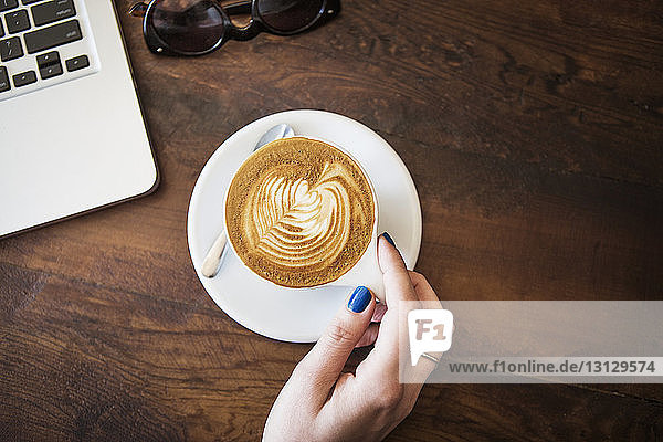 Beschnittenes Bild einer Hand mit Cappuccino auf Holztisch