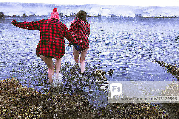 Rear view of female friends enjoying in lake during winter