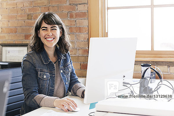 Lächelnde Geschäftsfrau schaut weg  während sie im Büro sitzt