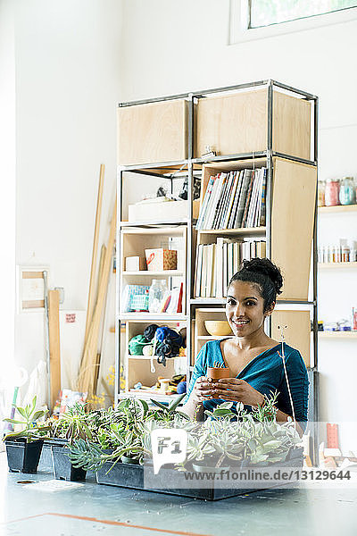 Porträt einer selbstbewussten Geschäftsfrau  die eine Topfpflanze hält  während sie im Büro gegen Regale steht
