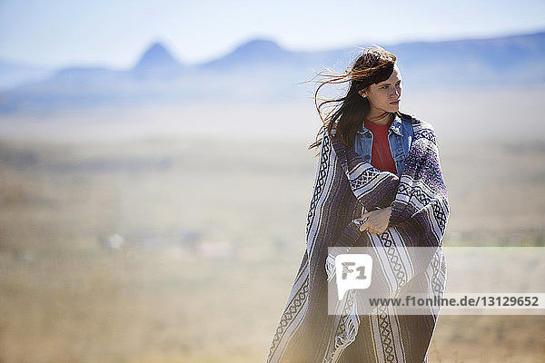 Thoughtful woman wrapped in blanket walking on field