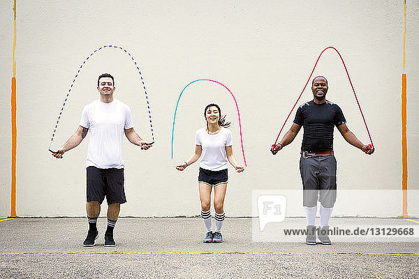 Glückliche Freunde spielen mit Sprungseilen auf der Straße an der Wand