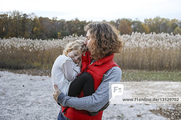Mutter küsst Tochter  während sie im Winter auf dem Feld gegen den Himmel steht