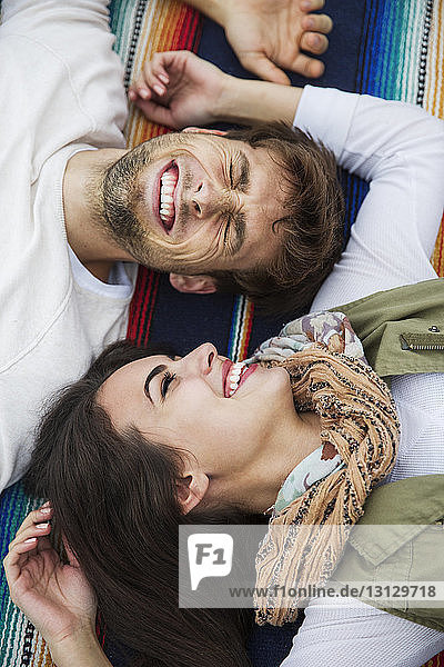 High angle view of cheerful couple lying on blanket at park