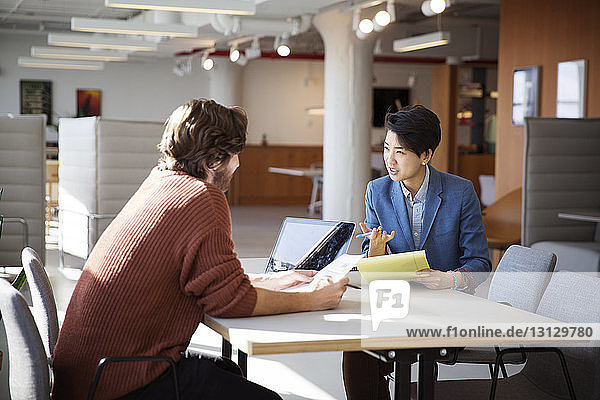 Businesswoman discussing with male colleague at table in office