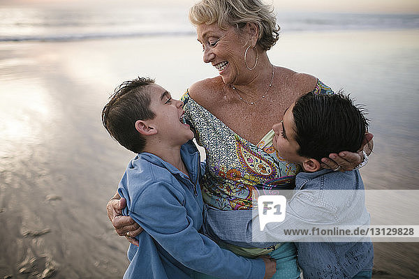 Happy grandmother with grandsons standing at beach during sunset