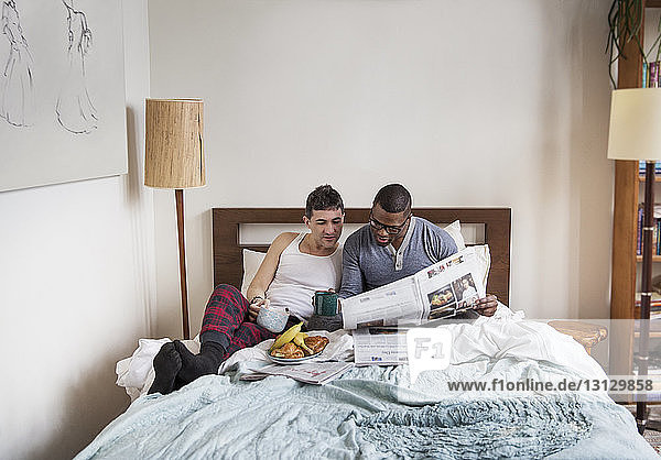 Multi-ethnic homosexual males reading newspaper in bedroom