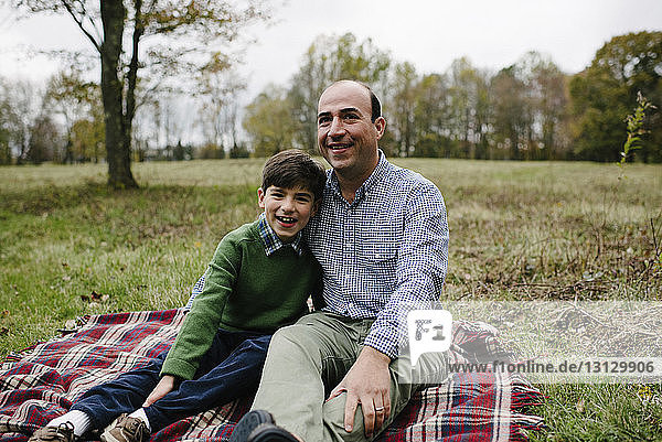 Portrait of father with son sitting on blanket against sky at park