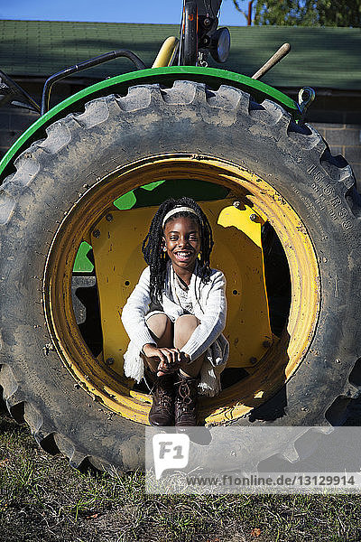 Porträt eines lächelnden Mädchens  das in einem Reifen auf einem Grasfeld sitzt
