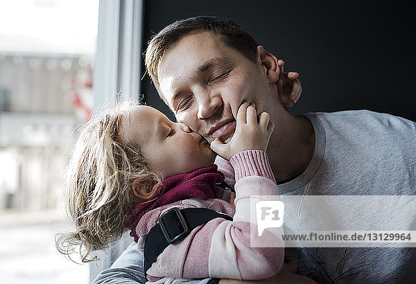 Daughter kissing father while sitting by window at home