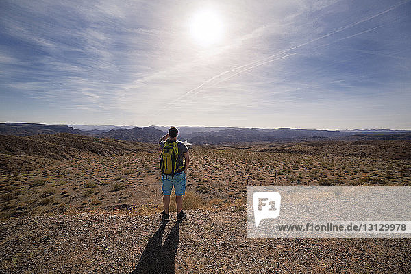 Rear view of hiker standing on field against sky during sunny day