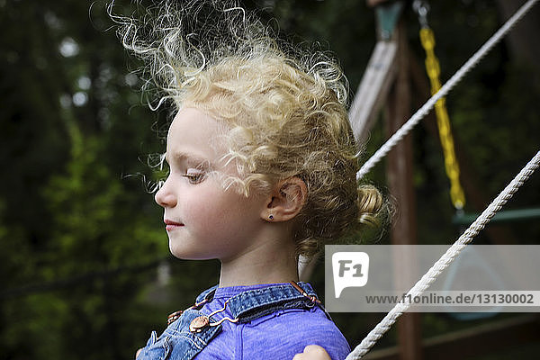 Side view of cute girl looking away while swinging at playground